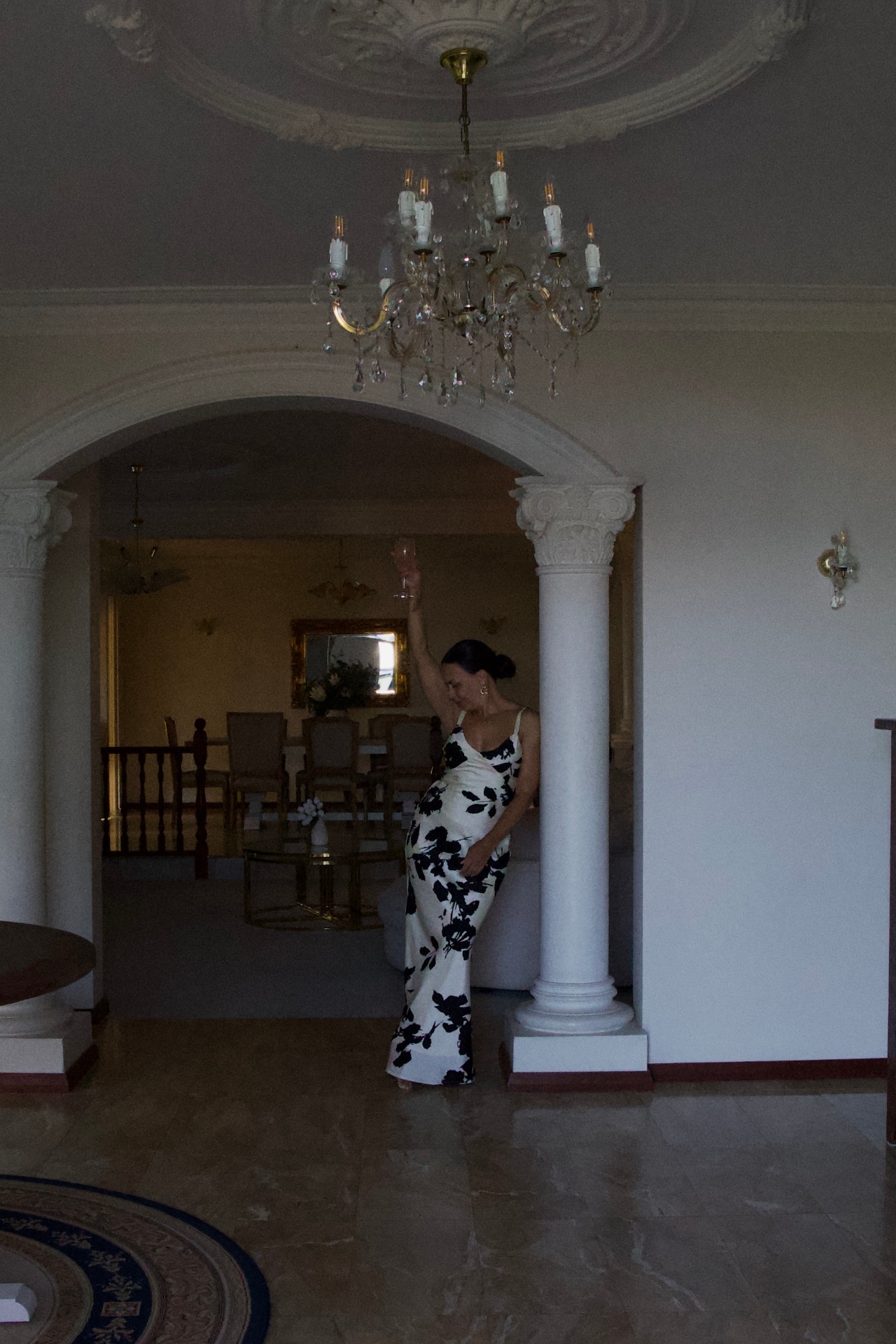 A woman in a floral gown beneath a crystal chandelier.