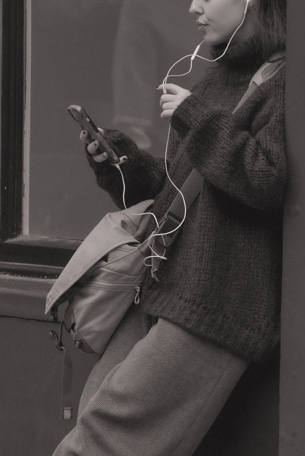 A woman leaning against a window with earphones in.