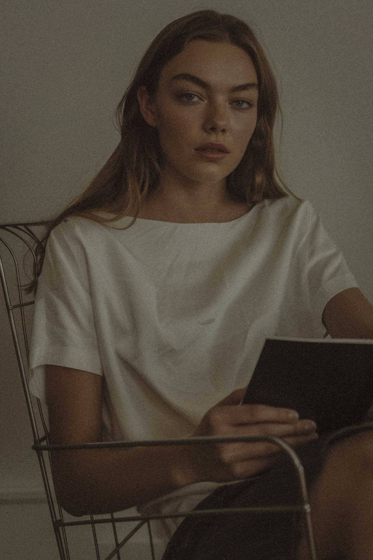 A woman seated in a wire chair, holding a notebook.
